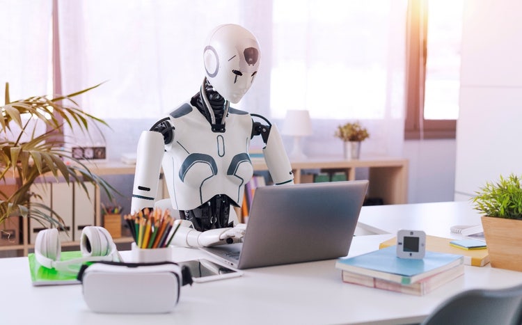A robot sitting at a desk with a computer Description automatically generated