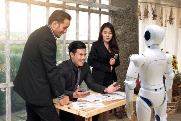 People in an office environment huddled around a desk including a robot