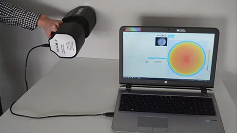 Eine Hand hält das Keysight Mini-Diff V2 an einer Wand, während es an einen geöffneten Laptop angeschlossen ist.