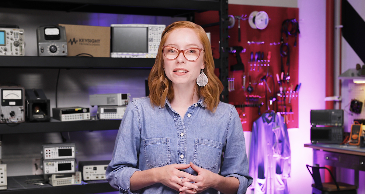 Keysight presenter wearing blue button down speaks while standing in front of shelves carrying Keysight products